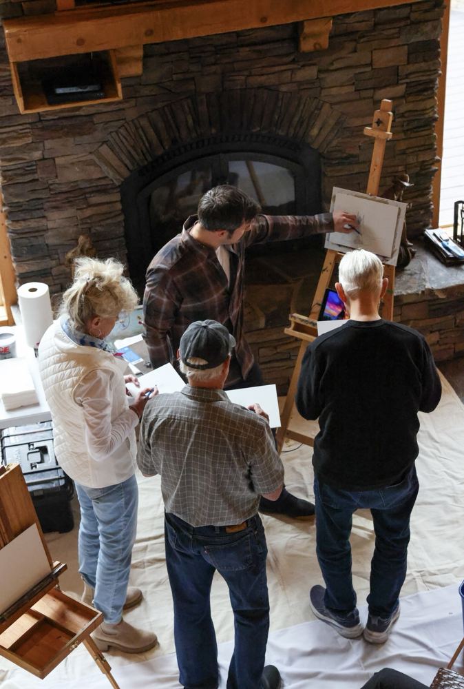 Painters gathered at an easel by a stone fireplace