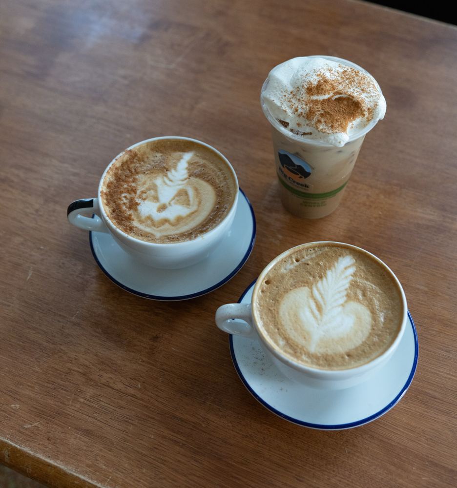Three lattes with leaf art on a wooden table