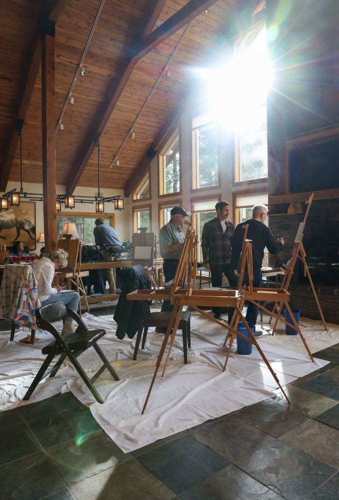 Easels set up in a sunlit lodge with a vaulted wood ceiling